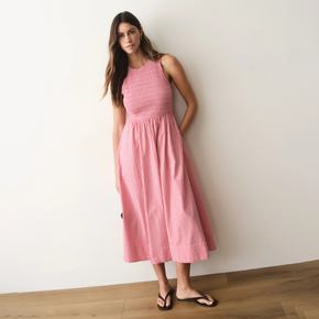 Woman wearing a pink striped dress standing against a white wall.