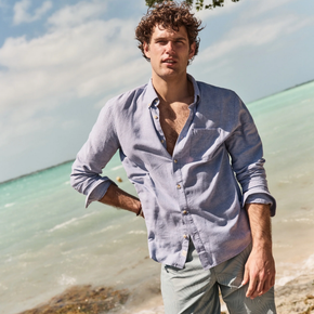 Man wearing a light blue shirt on a beach with ocean and sky in the background