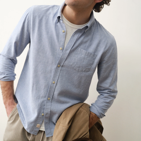 Person wearing a light blue button-up shirt with rolled-up sleeves, sitting against a plain background.