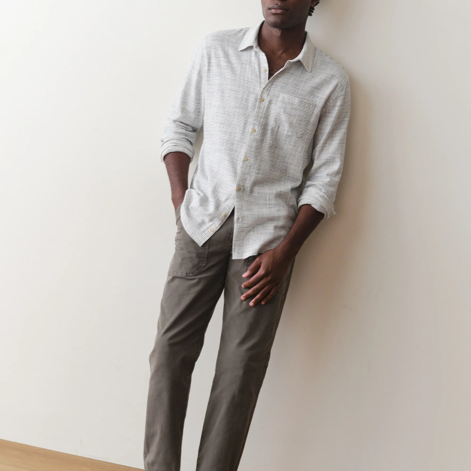 Man wearing a light gray shirt and dark gray pants against a white wall.