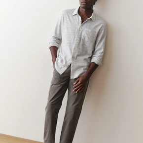 Man wearing a light gray shirt and dark gray pants against a white wall.