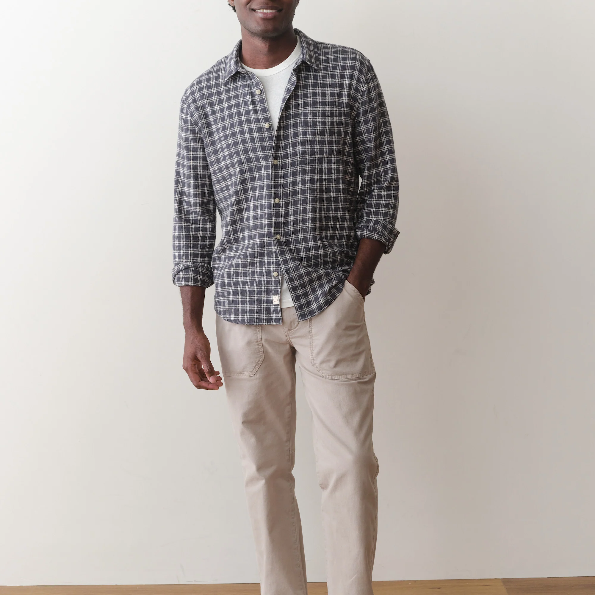 Man wearing a checkered shirt and beige pants against a plain background