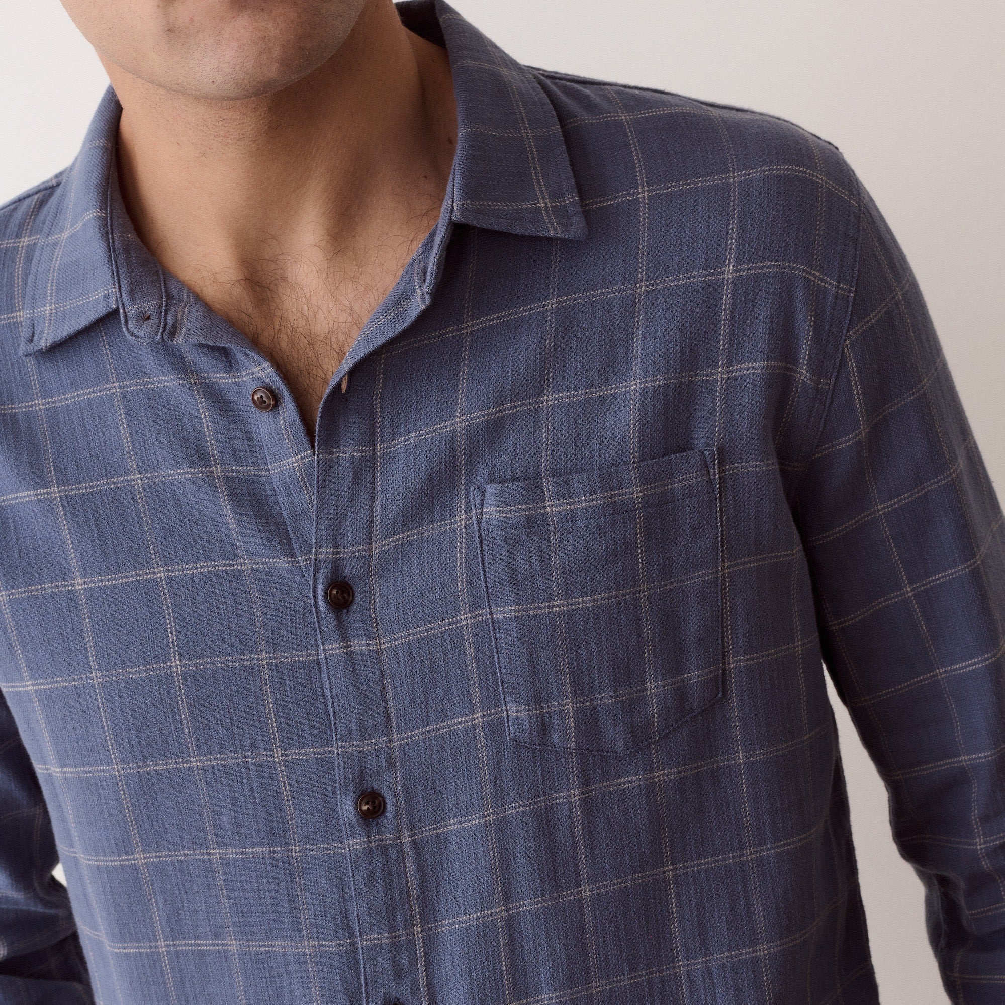 A close-up of a man wearing a blue long-sleeve plaid button-down shirt with a chest pocket, set against a plain light background.