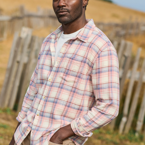 Man wearing a plaid shirt standing in a field with a wooden fence in the background