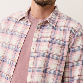 Man wearing a plaid shirt over a pink t-shirt against a plain background