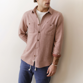 Man wearing a pink button-up shirt and blue pants against a white wall