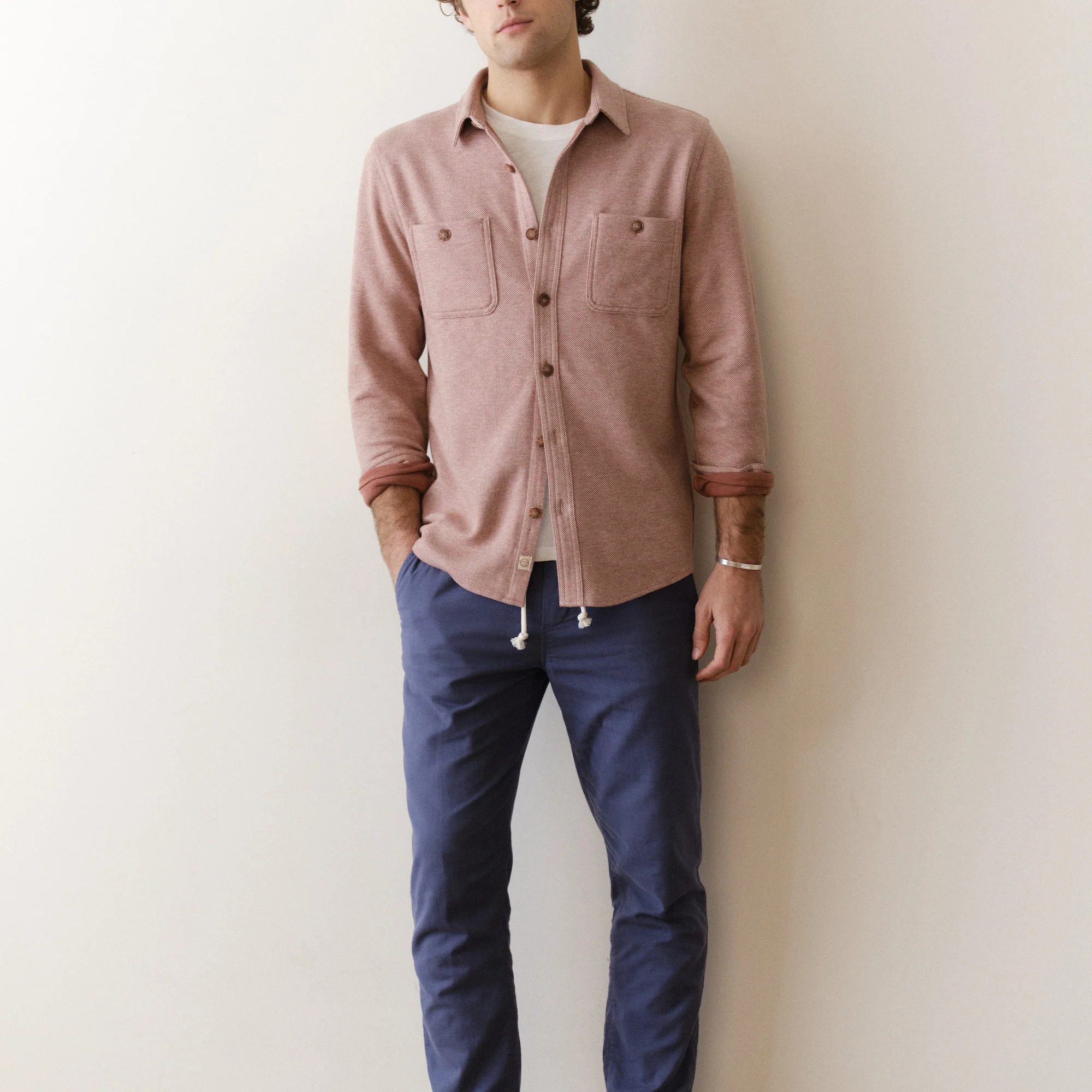 Person wearing a pink shirt and blue pants against a white wall