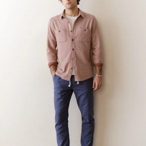 Person wearing a pink shirt and blue pants against a white wall