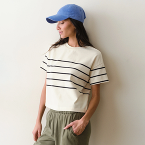 Woman wearing a white shirt with black stripes and green pants on a neutral background.