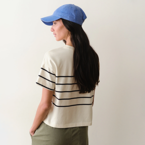 Woman wearing a white shirt with black stripes and green pants on a neutral background.
