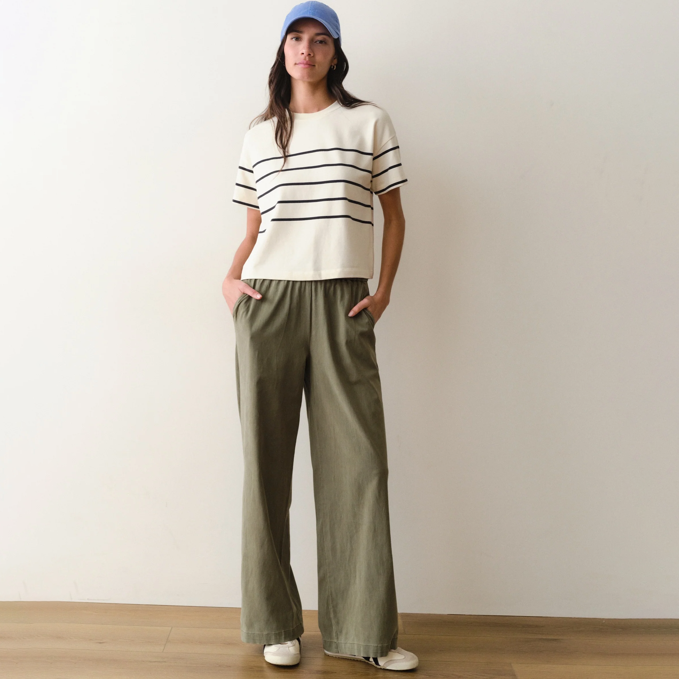 Woman wearing a white shirt with black stripes and green pants on a neutral background.