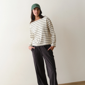 Woman wearing a black and white striped long sleeved tee and black pants on a neutral background.