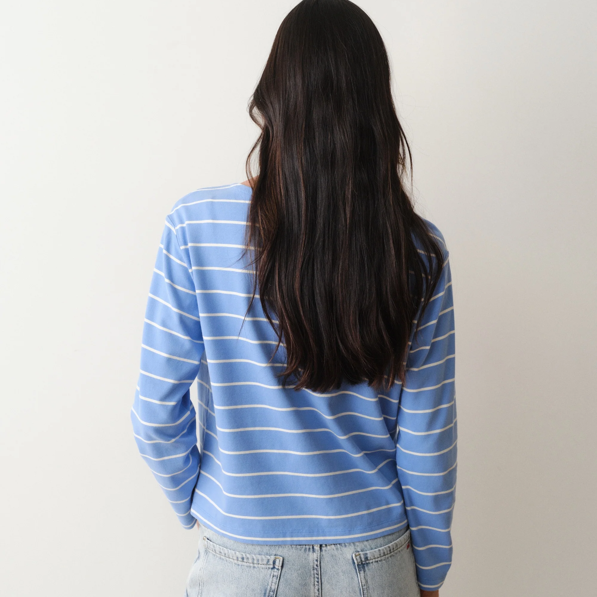 Person wearing a blue striped shirt and light jeans against a plain background