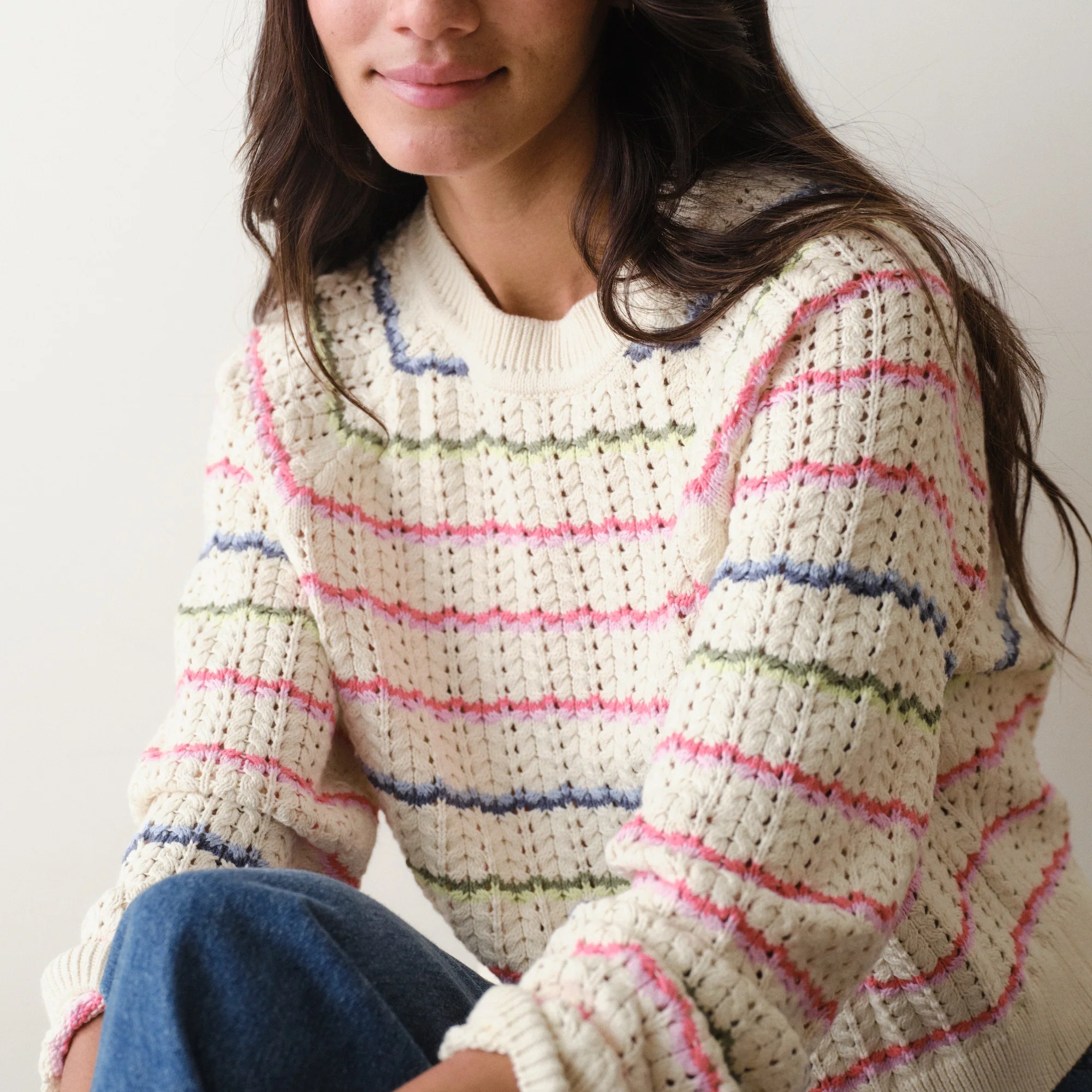 Person wearing a white sweater with colorful stripes sitting against a plain background