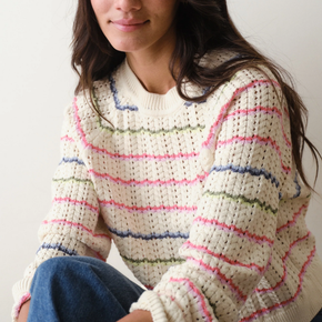 Person wearing a white sweater with colorful stripes sitting against a plain background