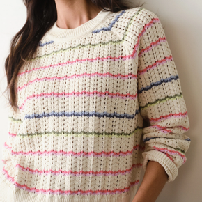 Person wearing a white sweater with colorful stripes against a neutral background