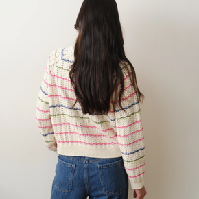 Person wearing a colorful striped sweater and blue jeans against a plain background