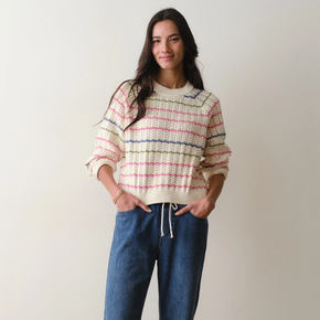 Woman wearing a striped sweater and blue jeans against a plain background