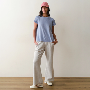 Woman wearing a light blue tee and white pants on a neutral background.