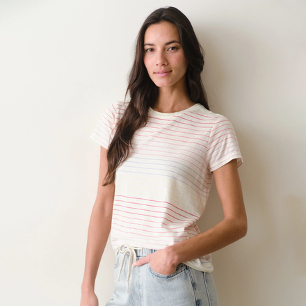 Woman wearing a rainbow stripe tee and jeans on a neutral background.