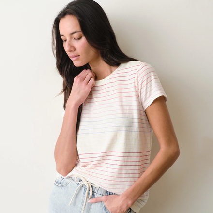 Woman wearing a rainbow stripe tee and jeans on a neutral background.