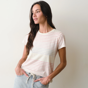 Woman wearing a rainbow stripe tee and jeans on a neutral background.