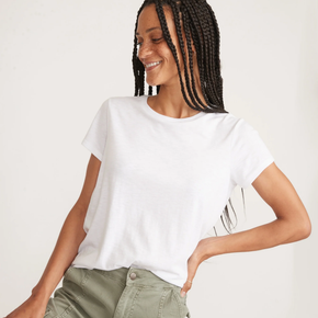 Woman wearing a white tee and green pants on a neutral background.