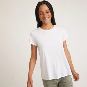 Woman wearing a white tee and green pants on a neutral background.