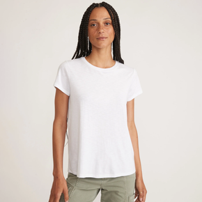 Woman wearing a white tee and green pants on a neutral background.