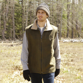 Man wearing a green vest and knit hat standing in a forested area