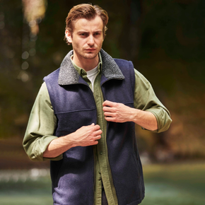 Man wearing a navy vest over a green shirt with a blurred natural background