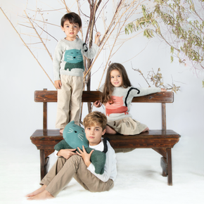 Three children sitting on a wooden bench with decorative branches in the background