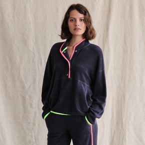 Sundry Faux Sherpa 90s Sweatshirt - model wearing navy blue faux sherpa sweatshirt with neon green and pink details around the cuffs, collar, and bottom, a large kangaroo pocket on the front, and snaps from the pocket to the collar on a neutral background