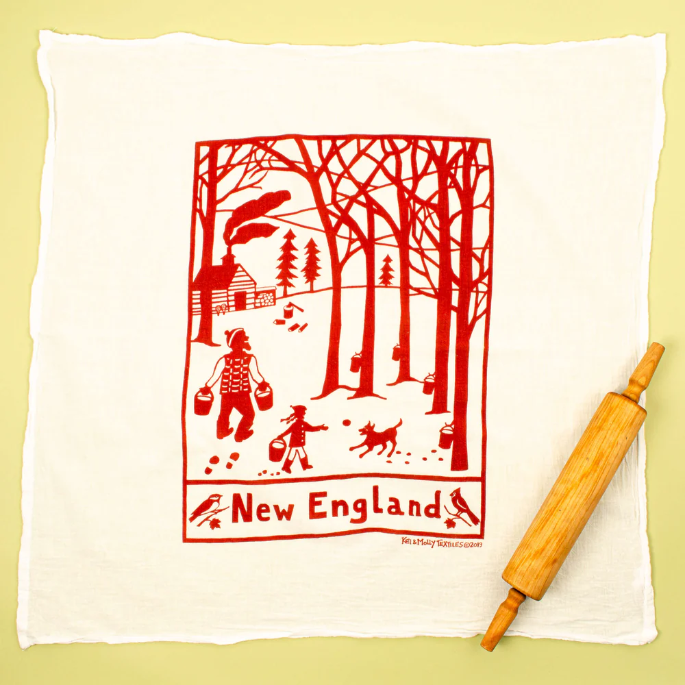 White towel with red New England scene design and wooden rolling pin on a yellow background