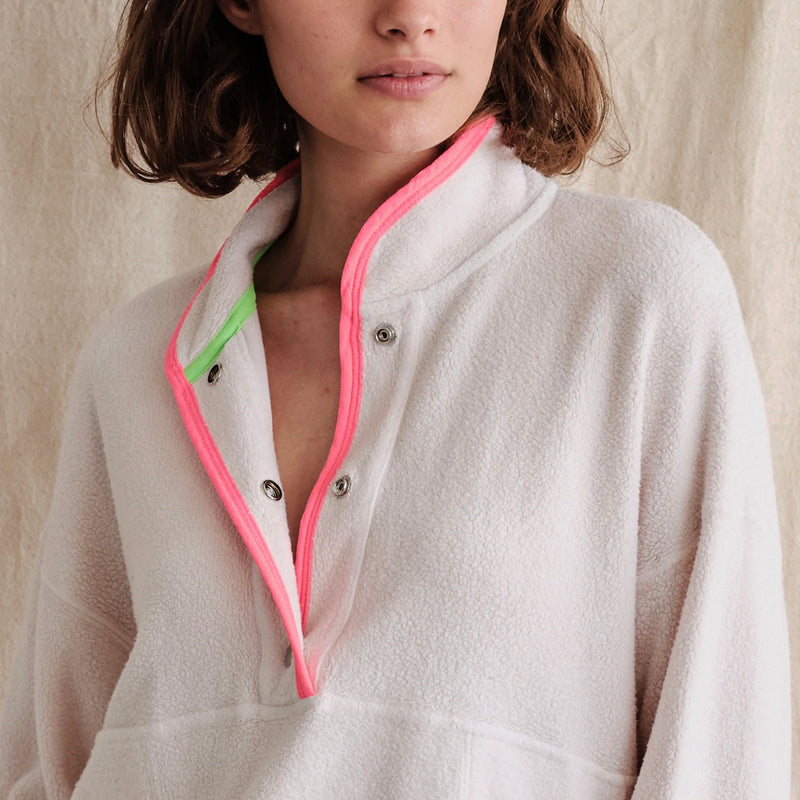 Sundry Faux Sherpa 90s Sweatshirt - model wearing white faux sherpa sweatshirt with neon green and pink details around the cuffs, collar, and bottom, a large kangaroo pocket on the front, and snaps from the pocket to the collar on a neutral background