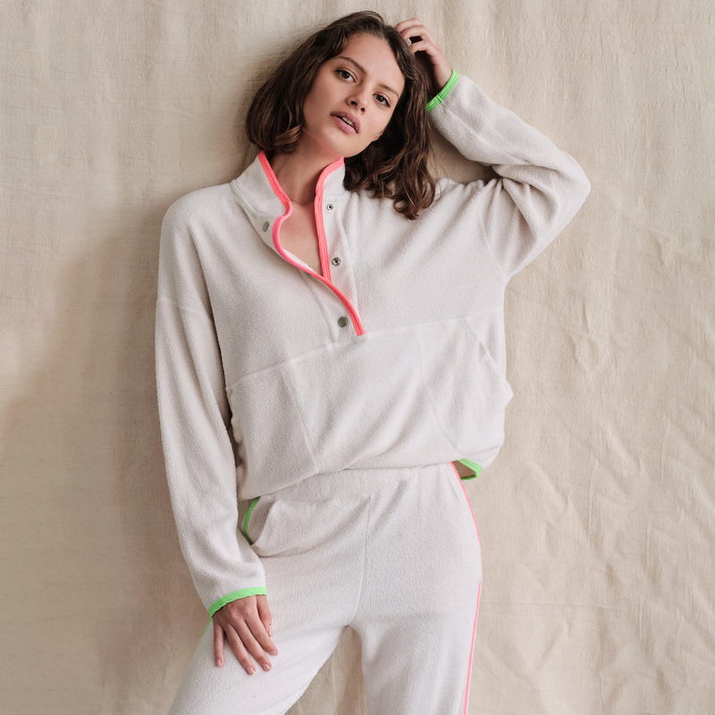 Sundry Faux Sherpa 90s Sweatshirt - model wearing white faux sherpa sweatshirt with neon green and pink details around the cuffs, collar, and bottom, a large kangaroo pocket on the front, and snaps from the pocket to the collar on a neutral background