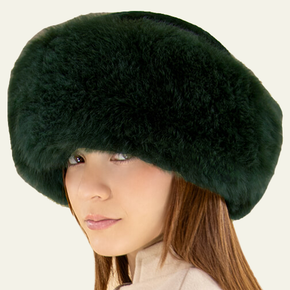 Person wearing a dark green fur hat with a beige background.