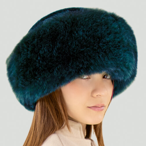 Person wearing a teal fur hat with a beige background.
