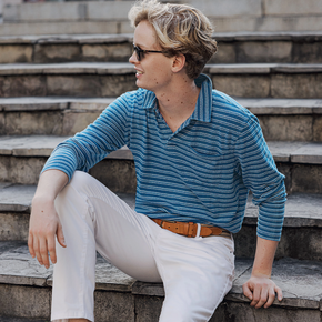 Man wearing a long sleeve blue striped polo and white pants.