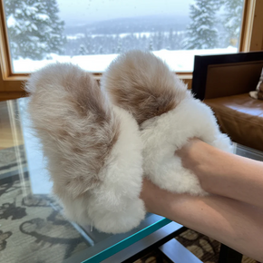 White fluffy slippers being held in a room with a window view of snow.