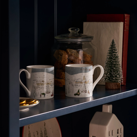 Two mugs on a shelf with decorative items including a jar, books, and a small Christmas tree.