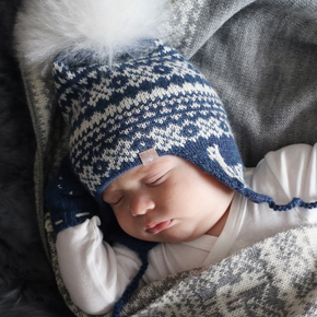 Baby sleeping in a basket wearing a blue and white patterned hat and matching gloves.