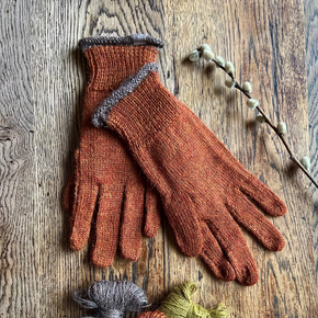 Pair of rust orange gloves with brown accents on a wooden surface.