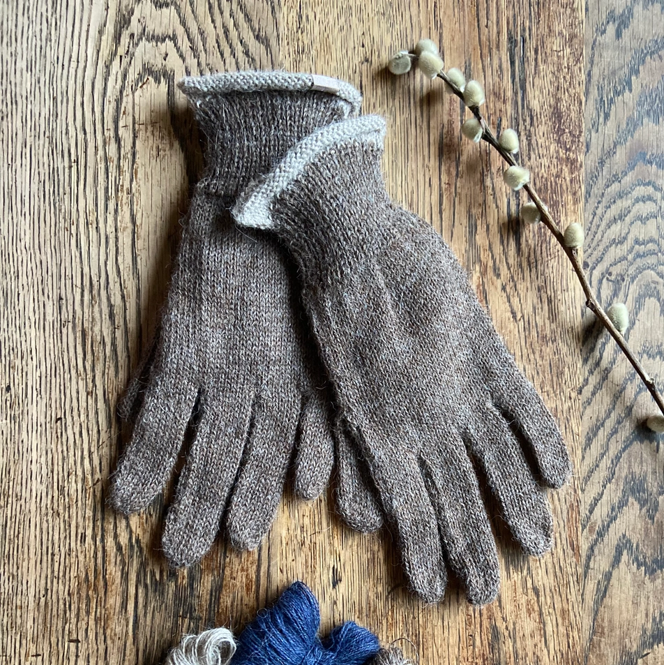 Pair of brown gloves with textured cuffs on a wooden surface, accompanied by small balls of yarn.