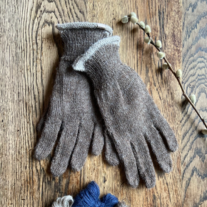 Pair of brown gloves with textured cuffs on a wooden surface, accompanied by small balls of yarn.