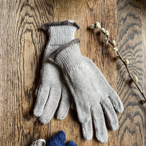 Pair of beige gloves on a wooden surface with small balls of yarn.