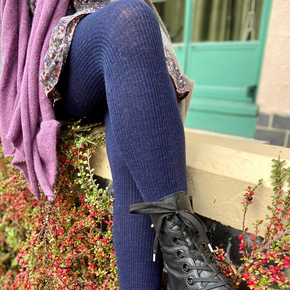 Person wearing black boots and blue leggings sitting on a plant with a blurred background