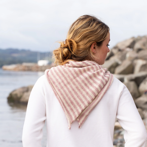 Woman wearing a pink striped scarf by a body of water with rocks.