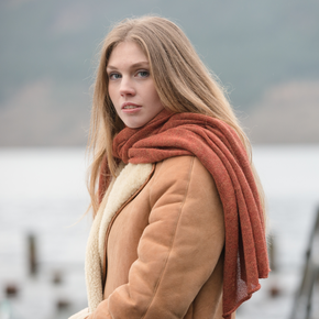 Woman wearing a brown coat and orange scarf by a lake