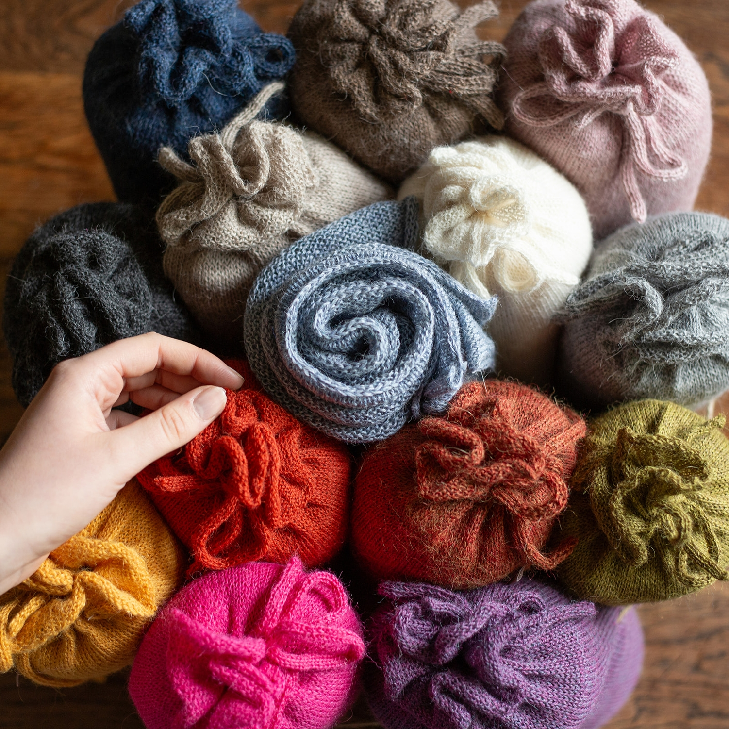 Hand reaching into a pile of colorful knitted yarn balls on a wooden surface